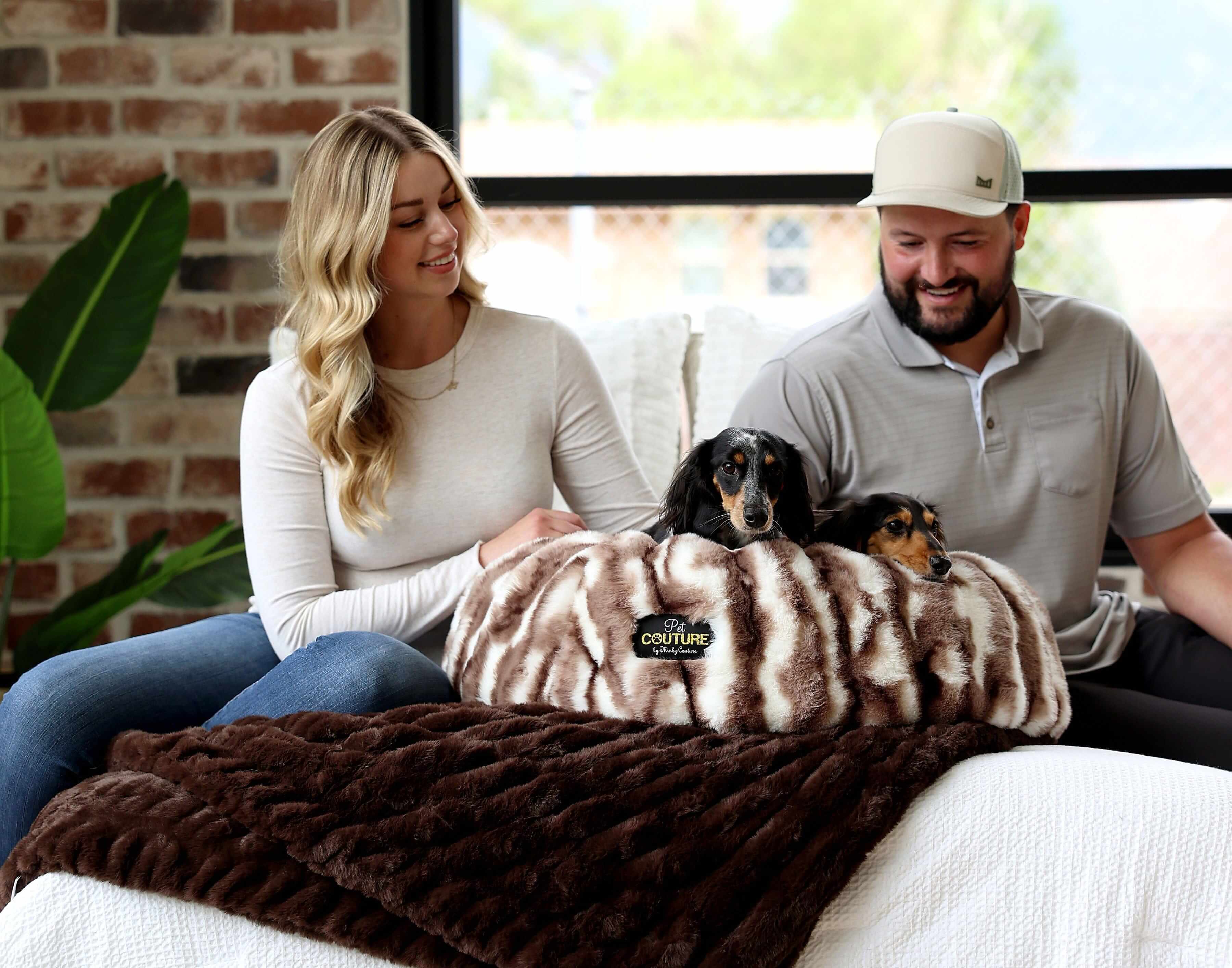 Couple sitting with dogs on Cloudy Day Brown Pet Bed featuring Minky Couture fabric in cozy setting.