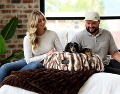Couple sitting with dogs on Cloudy Day Brown Pet Bed featuring Minky Couture fabric in cozy setting.