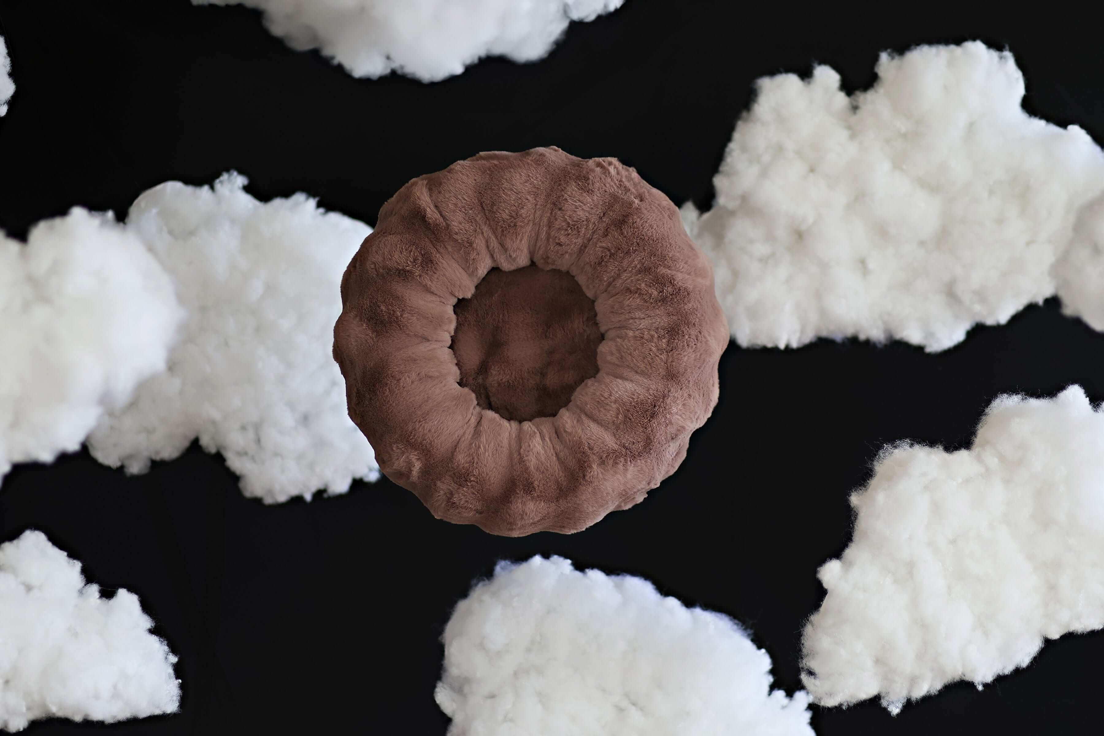 Minky Couture Milk Chocolate Pet Bed surrounded by fluffy clouds, showcasing its circular and cozy design.