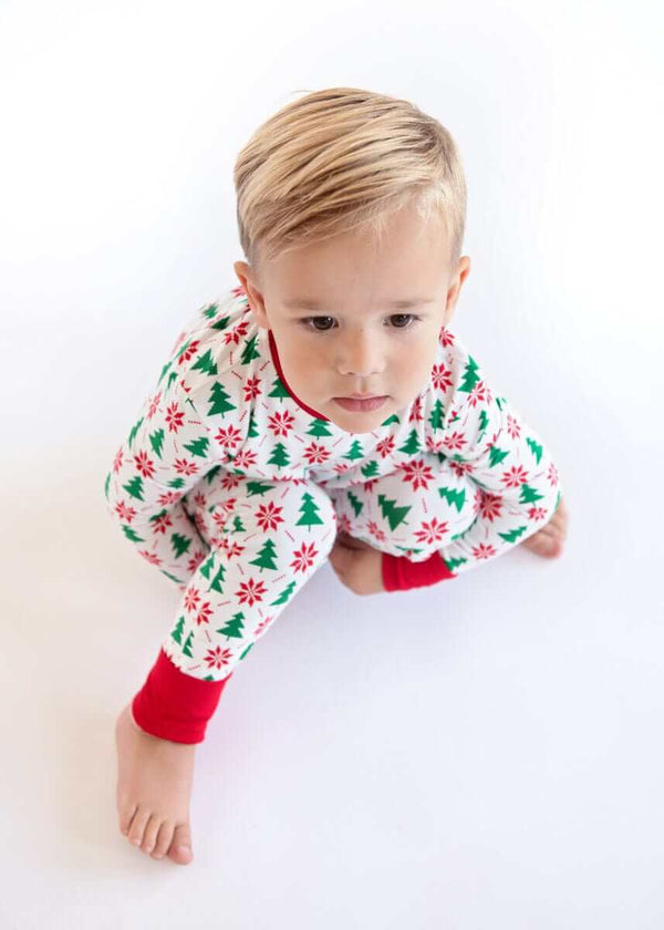 Toddler sitting on a white background wearing a holiday sleeper with holly print and red cuffs.