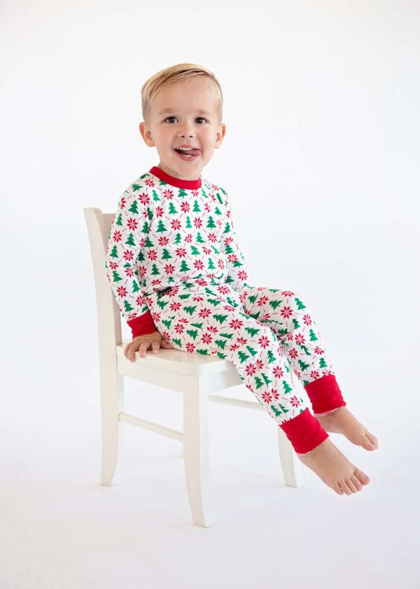 Toddler sitting on a chair wearing a Snug-Fitting Unisex Toddler Matching Set holiday sleeper with holly print and red cuffs.