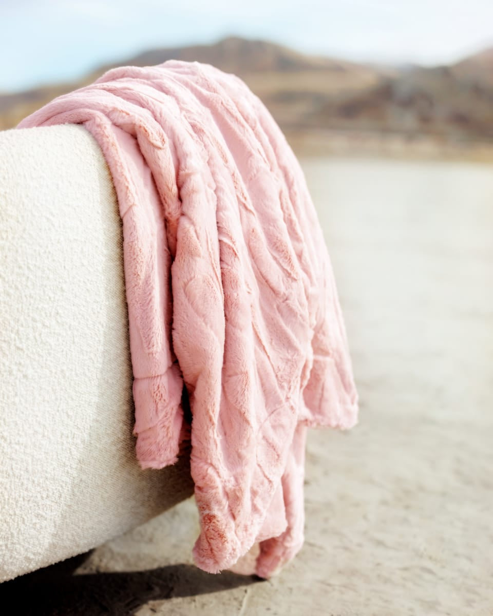 Pink textured blanket draped over a white surface with a blurred natural background