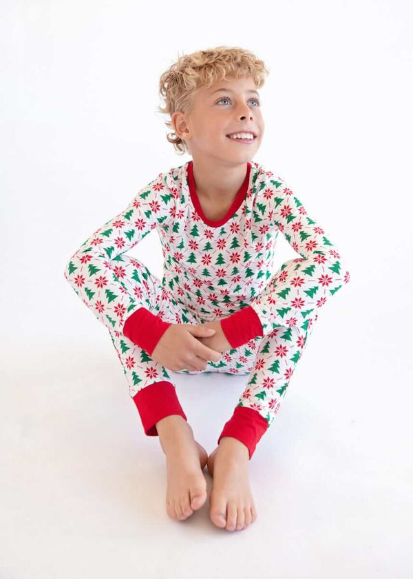 A smiling child in festive red-and-green holiday Snug-Fitting Unisex Tween Matching Set pajamas sitting.