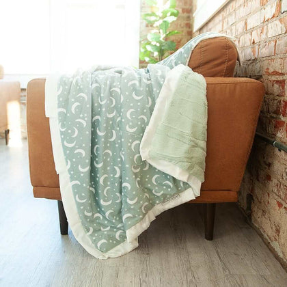 Twilight Sky Blanket draped over a cozy chair, featuring creamy stars and crescent moons on a sage green background.