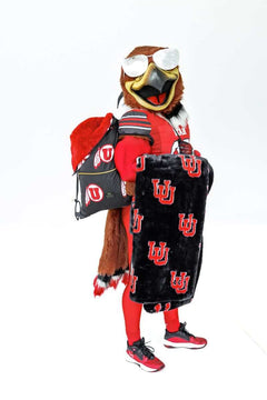 Mascot in red uniform holding black U logo  blanket and matching drawstring bag.