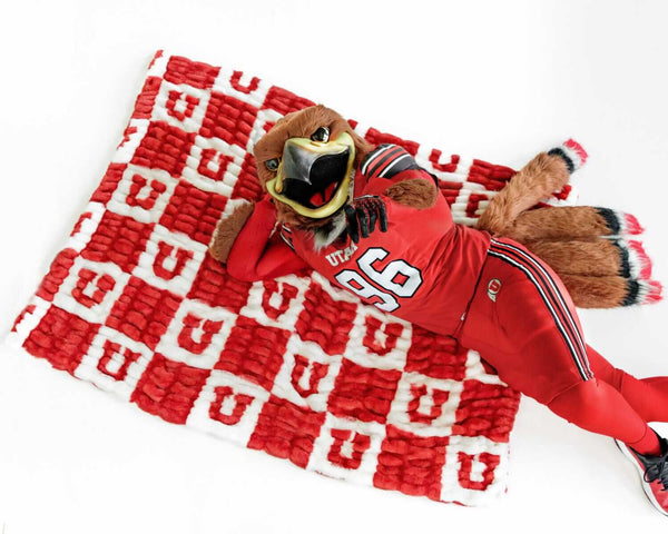 Minky Couture University of Utah Utes Blanket with mascot lounging on red and white checkered design.