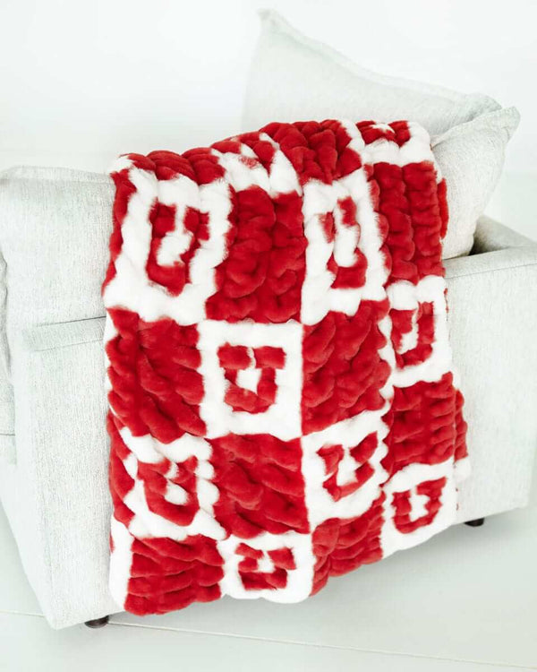 University of Utah Blanket Hugs draped over a couch, showcasing bold red and white checkered design with iconic logo.