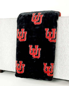 Black plush Minky Couture University of Utah blanket with red U logo draped over light gray sofa arm.