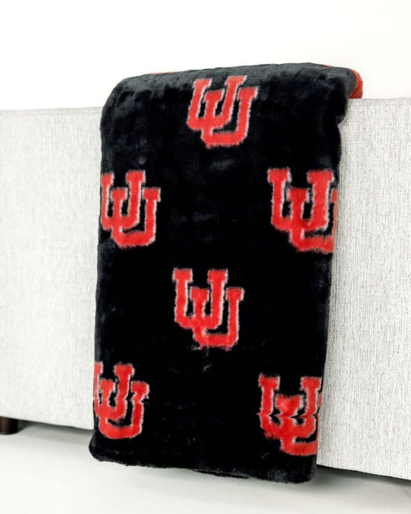 Black plush Minky Couture University of Utah blanket with red U logo draped over light gray sofa arm.