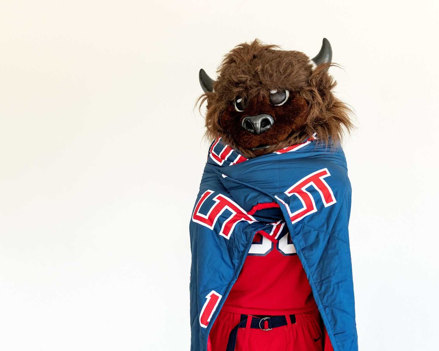 Utah Tech Trailblazers mascot wrapped in blue UT blanket over red uniform on white background.