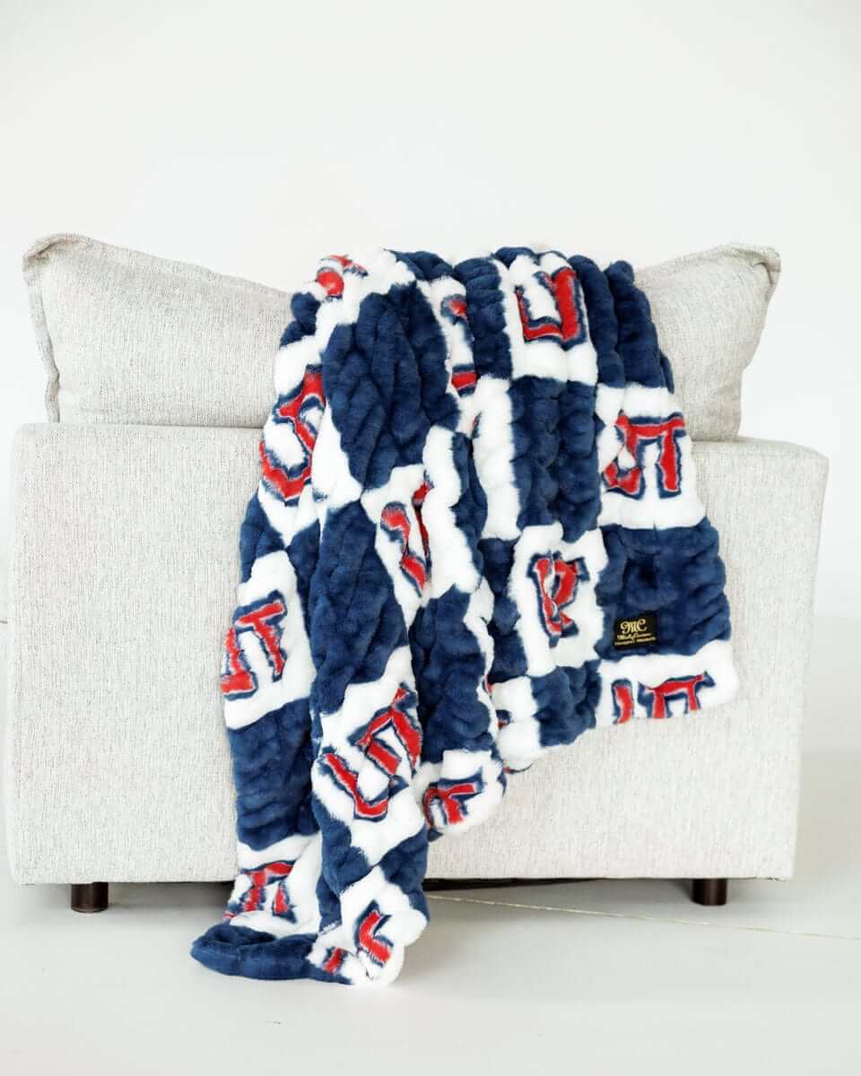 Blue and white Utah Tech Trailblazerscheckered plush blanket draped over light gray sofa indoors.