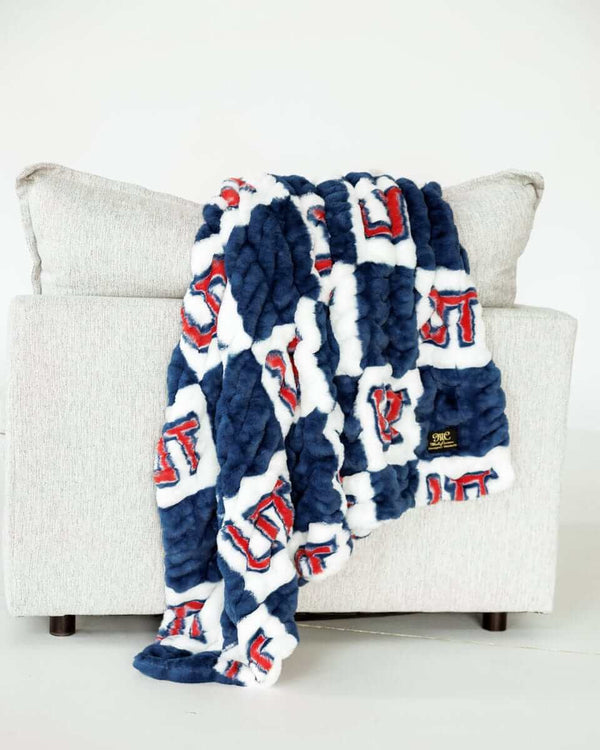 Blue and white Utah Tech Trailblazerscheckered plush blanket draped over light gray sofa indoors.