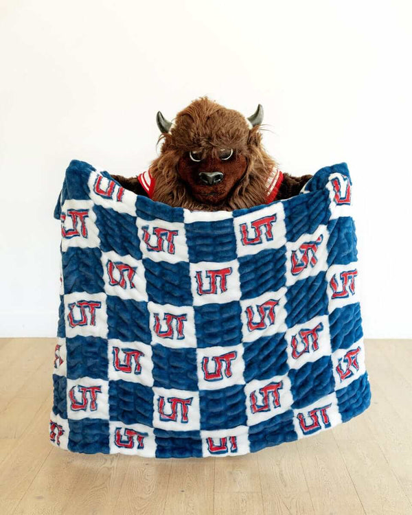 Buffalo mascot holding blue and white Utah Tech Trailblazers checkered plush blanket on white background.
