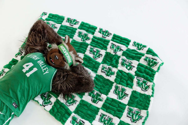 Utah Valley Wolverines mascot lounging on green and white checkered blanket with UV logo pattern.