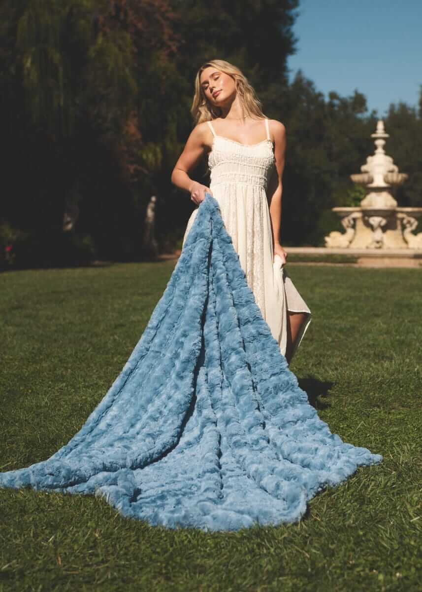 Model holding Ultra Sorbet Faded Denim Blanket on grassy outdoors, showcasing its rustic charm and cozy texture.