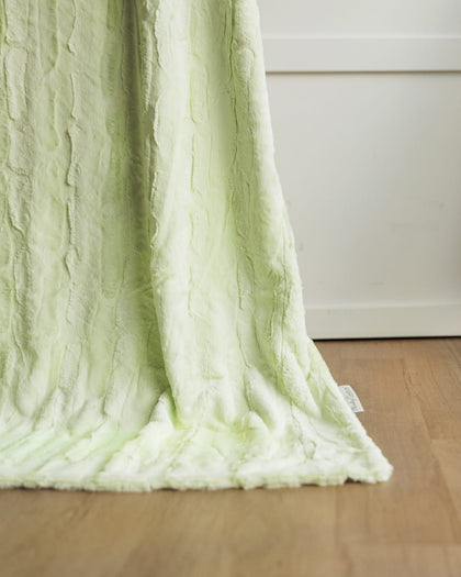 A Minky Couture Sorbet Lemon Lime blanket draped over the edge of a white chair in a room with a light wood floor.