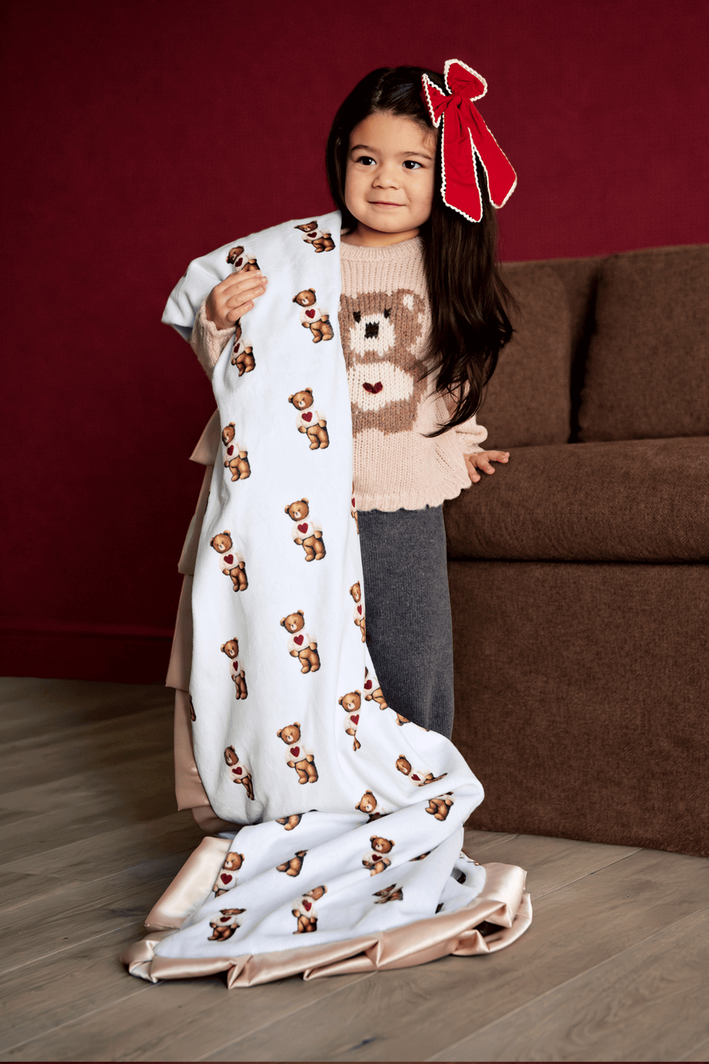 Child holding a long, Valentine teddy bear patterned blanket in a living room setting.