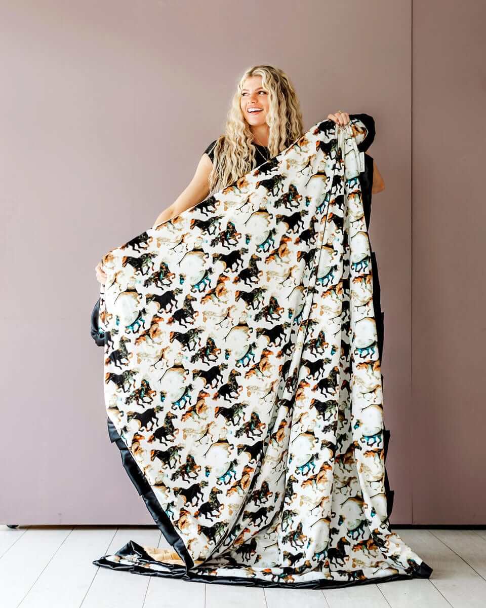 Stallion Blanket featuring watercolor horses on cream, held by a woman against a pink wall, ideal for cowboy themes.
