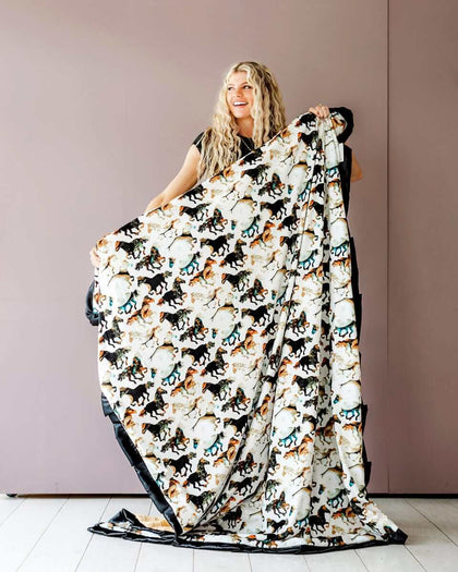 Stallion Blanket featuring watercolor horses on cream, held by a woman against a pink wall, ideal for cowboy themes.