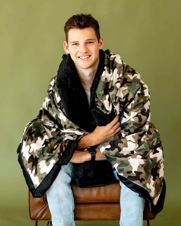 A smiling man wrapped in a stylish camo blanket, showcasing its cozy and plush design.