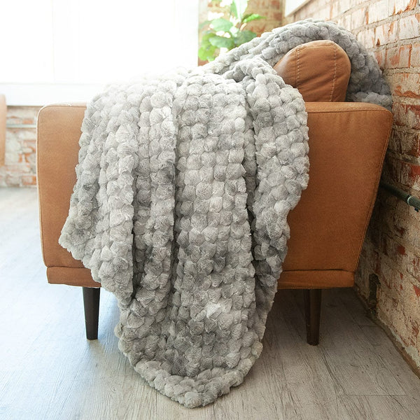 Light gray blanket hanging over the side of a brown leather couch,