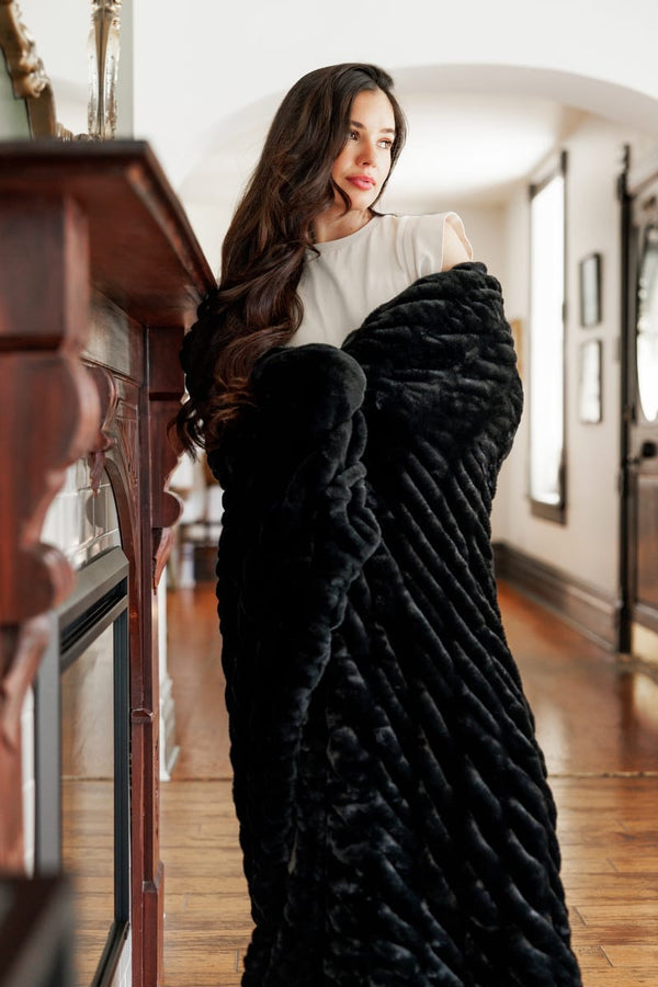 A woman elegantly draped in the Hugs Black Blanket, showcasing its plush texture and cozy appeal.