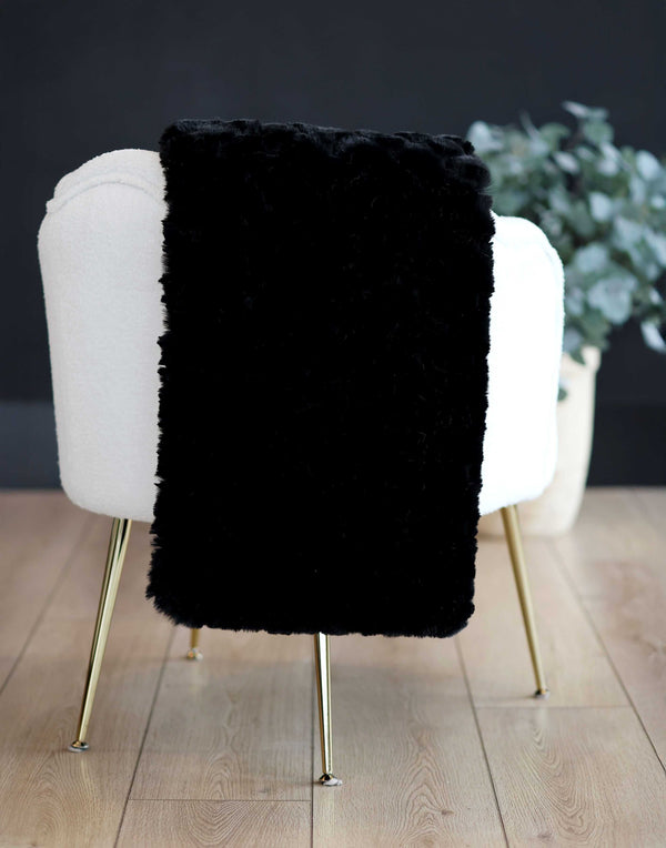 Black faux fur pet sized throw draped over a white chair with gold legs on a wooden floor.
