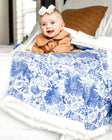 Baby girl laying on a Blue Willow floral patterned blanket on top of a bed.