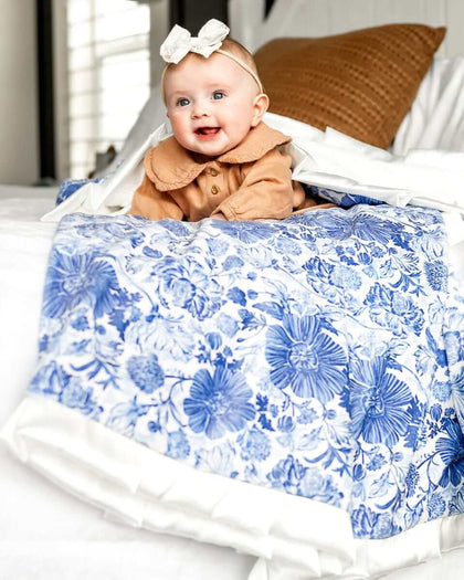 Baby girl laying on a Blue Willow floral patterned blanket on top of a bed.