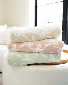 Minky Couture Bows Blankets, soft plush mint green, pink, and cream blankets stacked on a round table.