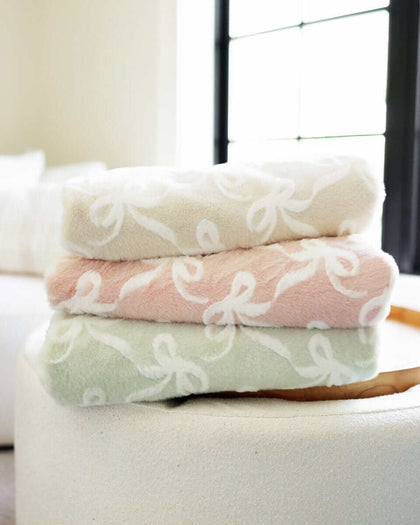 Minky Couture Bows Blankets, soft plush mint green, pink, and cream blankets stacked on a round table.