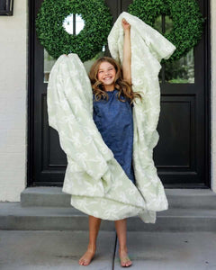 Bows Mint Blanket wrapped around a joyful girl outdoors with green wreaths, showcasing its soft texture and charming design.