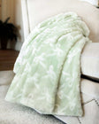 Minky Couture Bows Mint Blanket draped over a sofa, showcasing its soft sage green hue and embossed bow pattern.