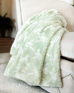 Minky Couture Bows Mint Blanket draped over a sofa, showcasing its soft sage green hue and embossed bow pattern.
