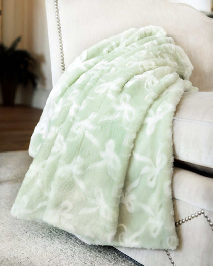 Minky Couture Bows Mint Blanket draped over a sofa, showcasing its soft sage green hue and embossed bow pattern.