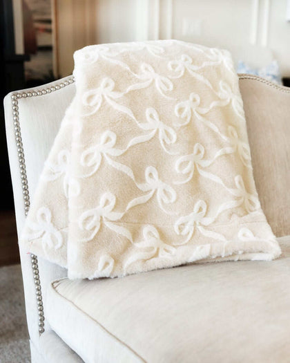 Bows Sand Blanket draped over a chair showcasing its plush fabric and embossed bow pattern.