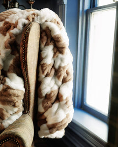 Hugs Check Milk Chocolate Blanket draped over a chair, showcasing its soft, checkered pattern and inviting comfort.