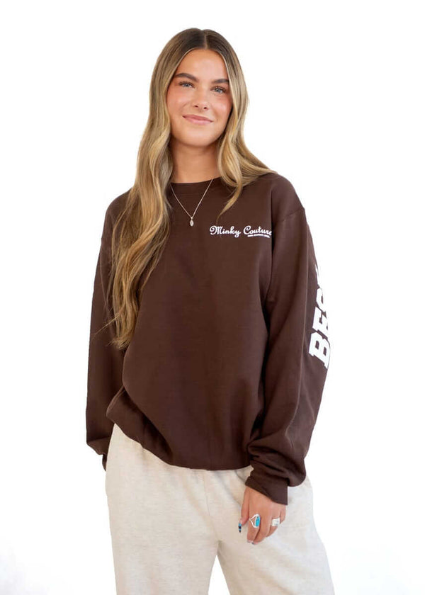 Model wearing a brown Hugs Chocolate Minky Couture sweatshirt with logo on the front.