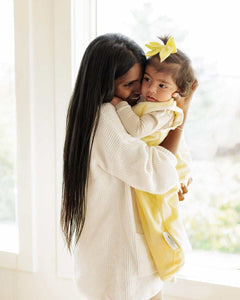 Woman smiling carrying a baby girl with a Minky Couture butter yellow wearable blanket.