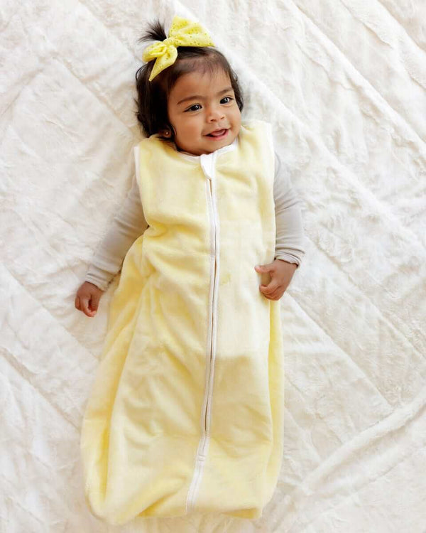 Smiling baby girl lying with a Minky Couture butter yellow wearable blanket.