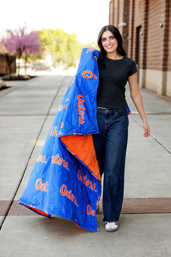 A woman walking outdoors with the Florida Gators Hooded Stadium Blanket, showcasing its vibrant blue and orange colors.