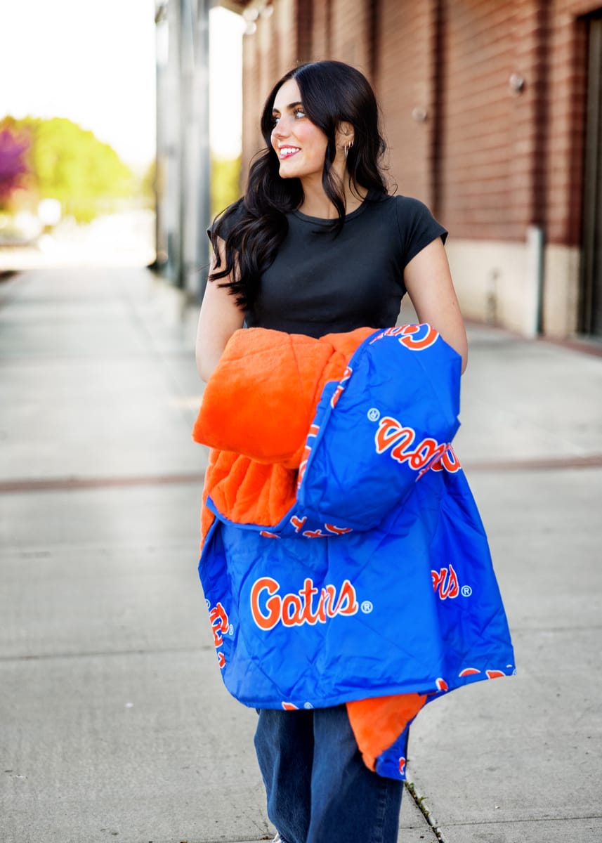 Woman wearing Florida Gators Hooded Stadium Everywhere Blanket while walking outdoors, showcasing team pride.