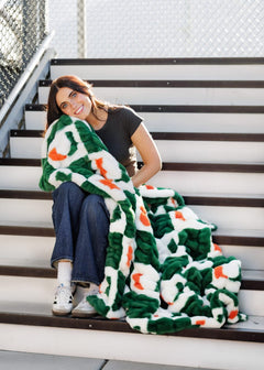 Miami Hurricanes Blanket wrapped around a smiling woman on stairs, showcasing team spirit and cozy comfort.