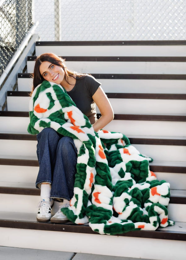 Miami Hurricanes Blanket wrapped around a smiling woman on stairs, showcasing team spirit and cozy comfort.