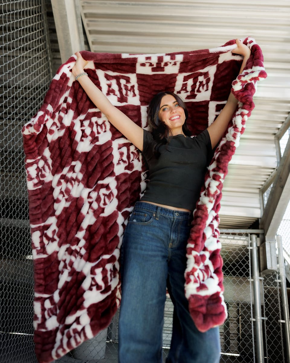Hugs Texas A&M Aggies Blanket showcased by a smiling woman in a checkered design, perfect for cozy lounging.
