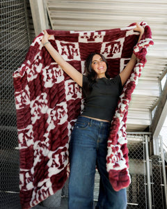 Hugs Texas A&M Aggies Blanket showcased by a smiling woman in a checkered design, perfect for cozy lounging.