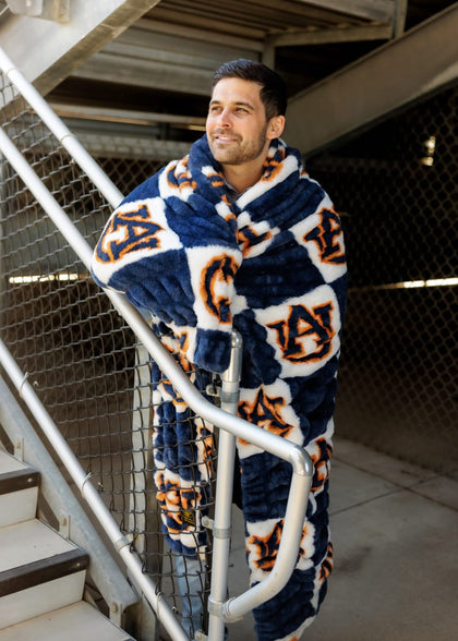 A man wrapped in a Hugs Auburn Tigers Blanket, showcasing team spirit in deep blue and orange colors.