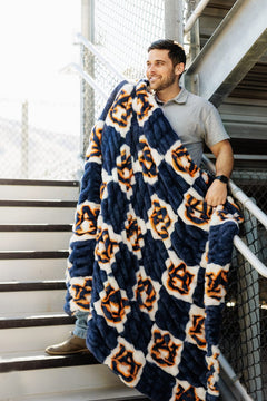 Auburn Tigers Blanket wrapped around a man on stairs, showcasing deep blue and checkered Auburn logo design.