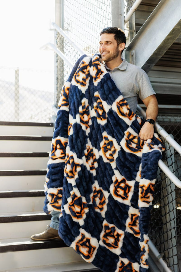 Auburn Tigers Blanket wrapped around a man on stairs, showcasing deep blue and checkered Auburn logo design.