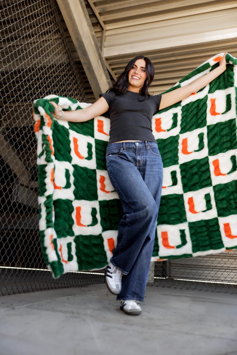 A happy woman showing off a Miami Hurricanes Blanket with a green and white checkered pattern.